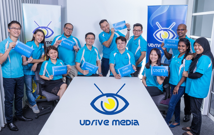 UDrive Media colleagues gathered around the company logo in the office